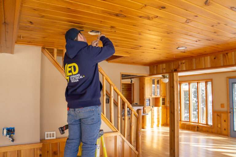 Electrician on ladder installing recessed LED downlight in wooden residential ceiling