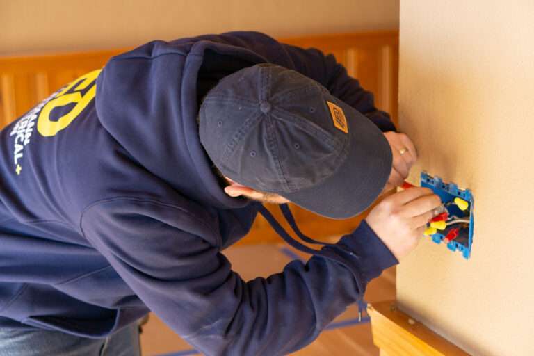 Lehmann electrician connecting wires in a blue electrical box on an interior wall
