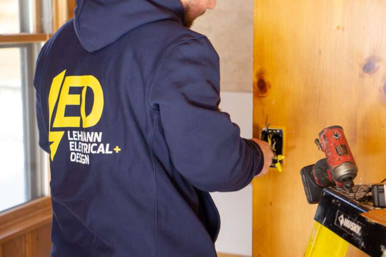 Lehmann electrician installing black outlet into wooden wall stud with cordless drill