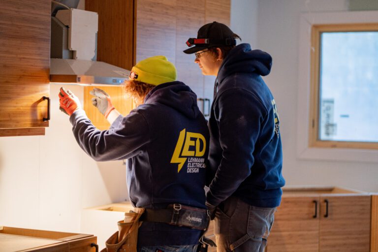 Two electricians in branded work gear inspecting wiring during a renovation