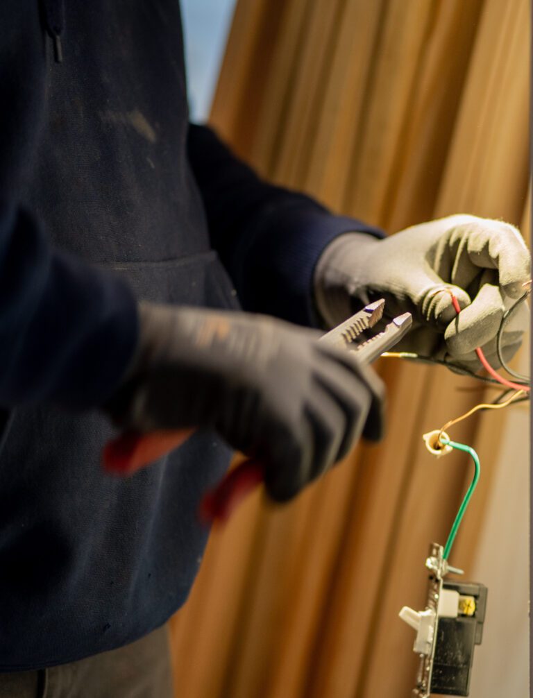 Electrician in work gloves inspecting and repairing a wall outlet with green and red wires