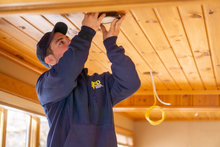 Electrician installing recessed light fixture into wooden ceiling