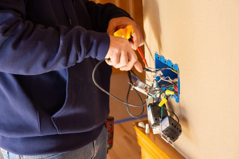 Electrician installing wires into a blue outlet box on a residential wall