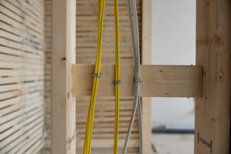 Yellow and gray electrical cables clamped to wooden cross-brace during residential framing rough-in