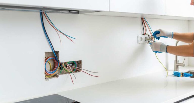 Electrician installing wiring into wall outlet box during kitchen remodeling project