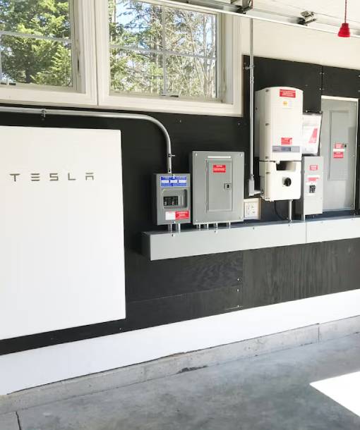 Tesla Powerwall battery storage unit installed on black wall with electrical breaker panels and interconnection equipment