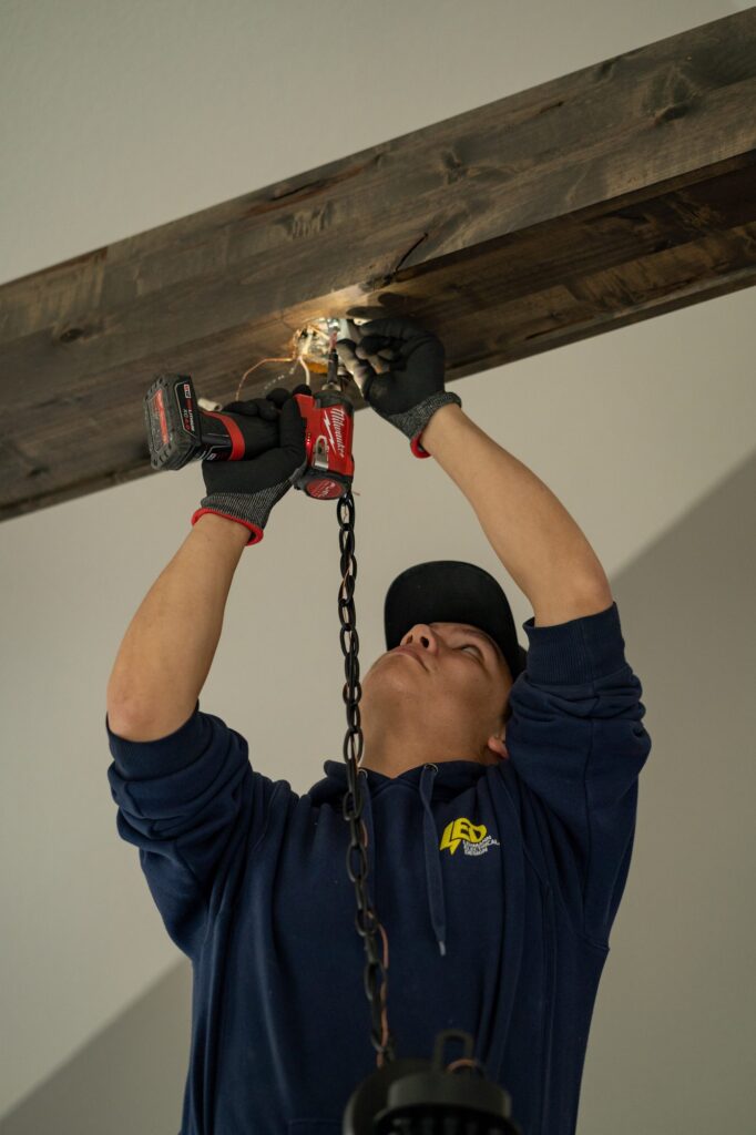 Electrician installing a chain-hung light fixture to a wooden beam with a power drill
